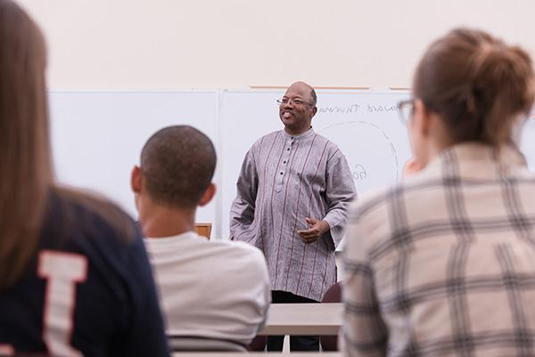 在宗教研究课上，一位面带微笑的男教授在白板前给一群学生上课