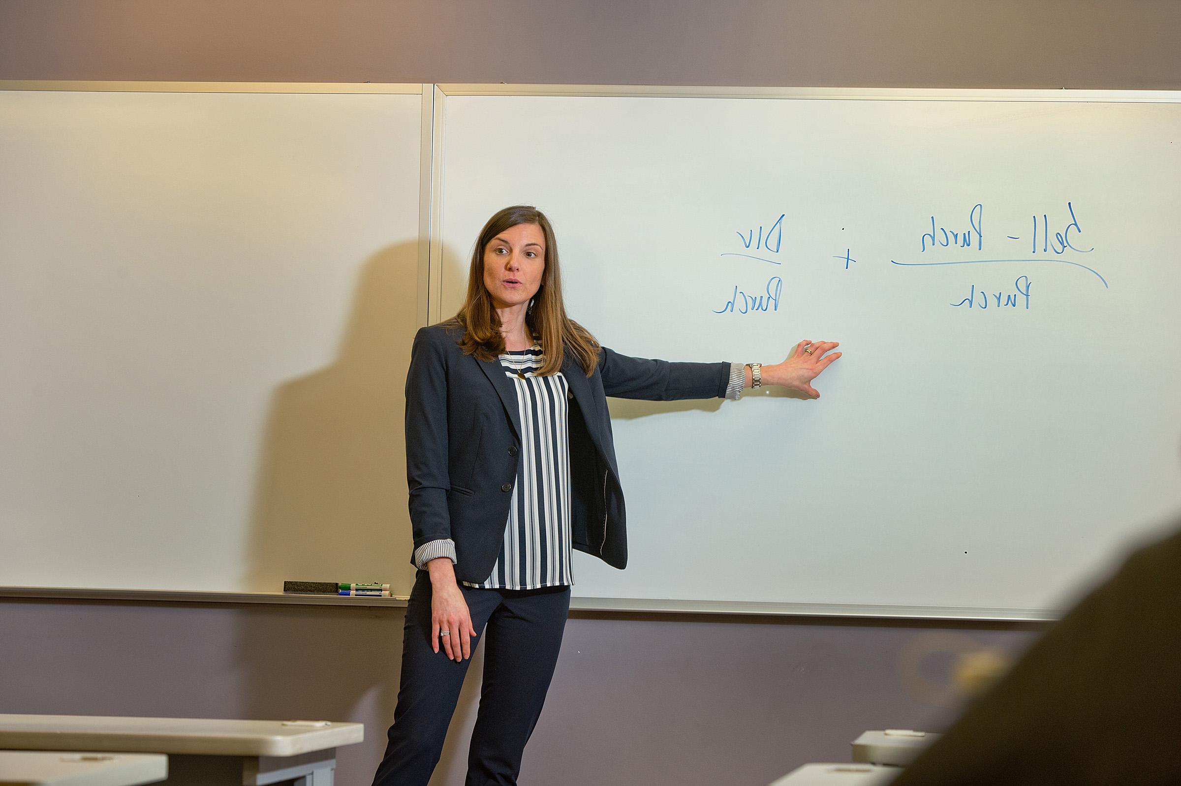 Professor teaching a class while pointing at a whiteboard 